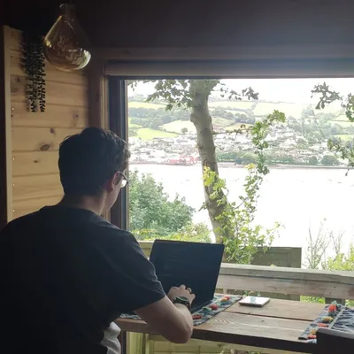 A photo of myself sat coding at a table overlooking the sea